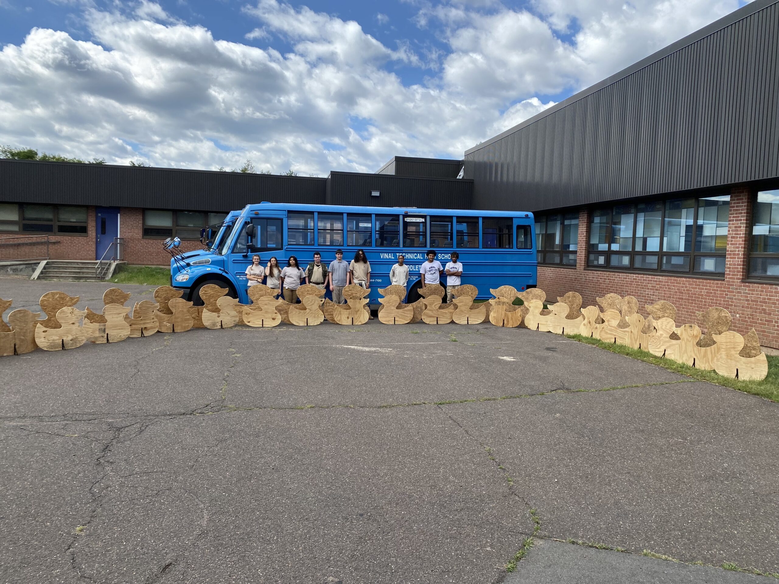 Vinal Tech Carpentry students standing in front of the blue production bus with their cut-outs of ducks.